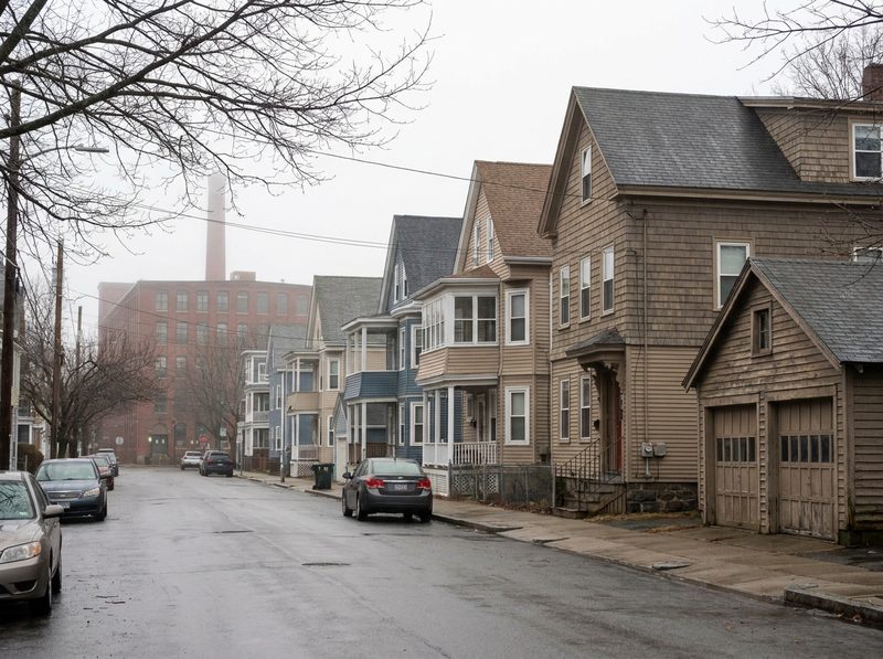 A Lowell mill-town street of triple-deckers and colonials, a brick mill beyond