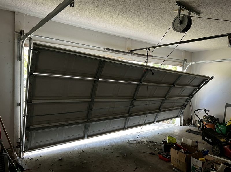 A sectional garage door hanging off its track, one side dropped and the cable slack