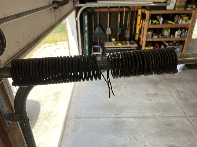 A snapped torsion spring on the shaft above a garage door, the break clearly visible